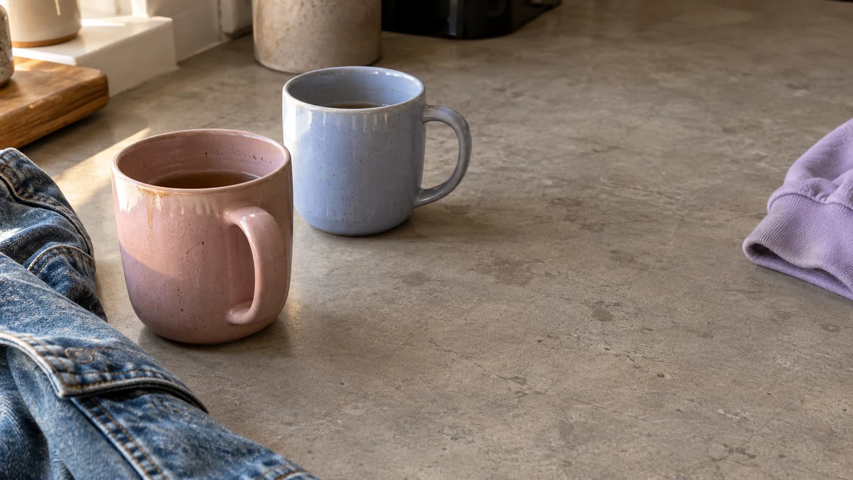 Two mugs beside a denim jacket and lavender hoodie, ready for a conversation.